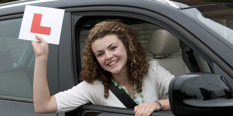 Girl leaning out of drivers seat and holding up learner plate