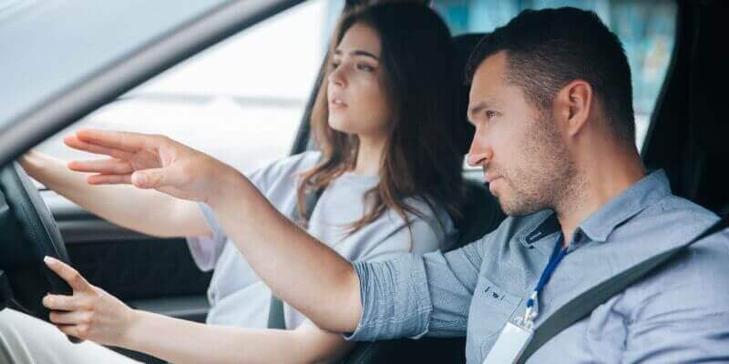 Instructor gesturing ahead in the car to guide the girl driving