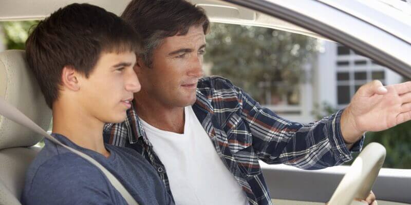 Two men in car with one gesturing ahead