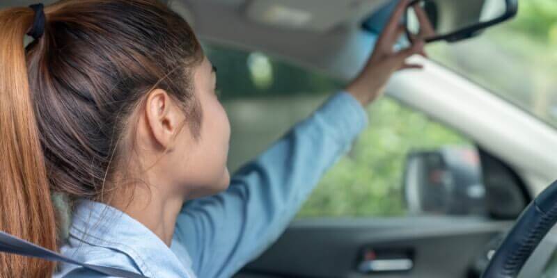 Girl reaching to adjust her rearview mirror