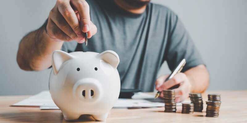 Person writing and putting coins into a piggy bank
